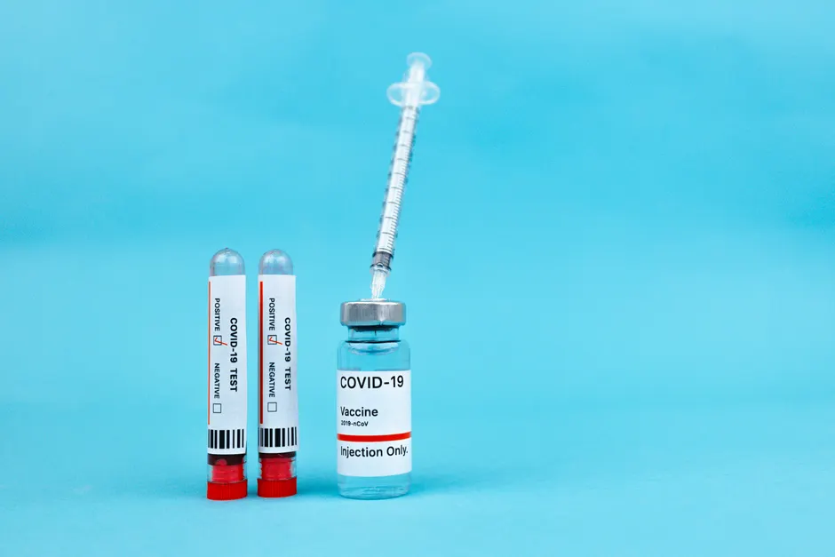 Vaccine vial and blood test tubes labeled COVID-19 on a blue surface, representing healthcare progress.