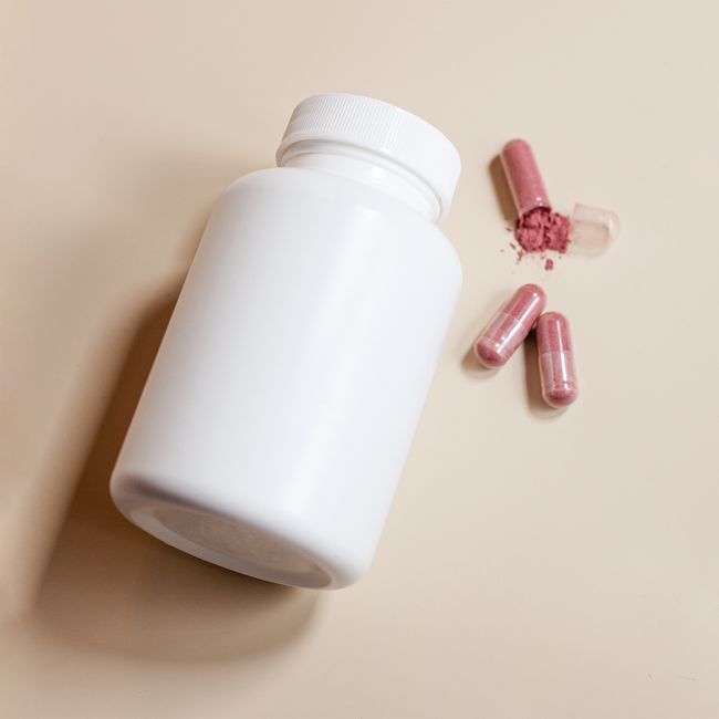 White pill bottle with spilled pink capsules containing powder, shot on a neutral background.