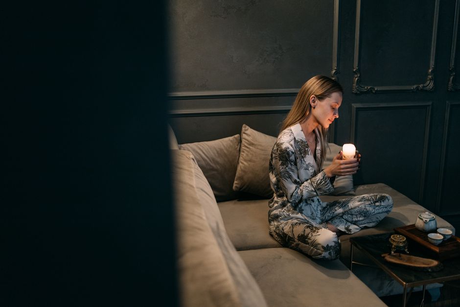 Le silence total est-il vraiment bon pour le cerveau? Woman in pajamas holding a candle, sitting on a cozy couch in a serene room.