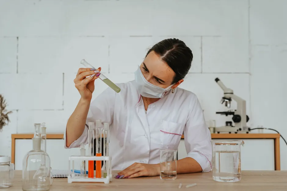 Les médiums peuvent-ils vraiment communiquer avec les morts? Woman scientist in lab coat examining a test tube with chemical solution, wearing safety mask.