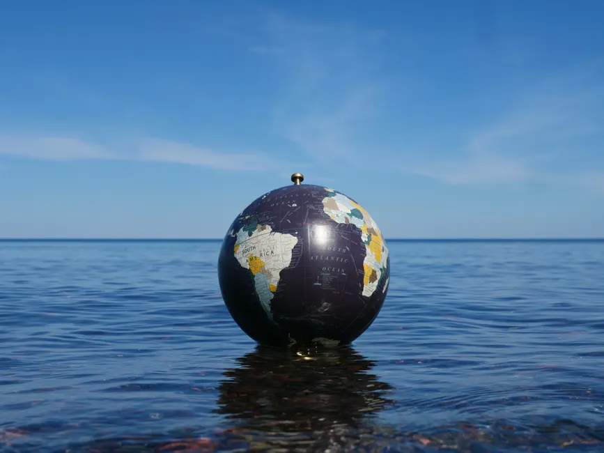 Saturne flotterait-elle vraiment dans l’eau? Le calcul qui piège l’intuition World globe floating on calm ocean water with clear blue sky background, symbolizing global environment concepts.